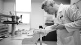 Person in a laboratory setting wearing a white coat, working with equipment.